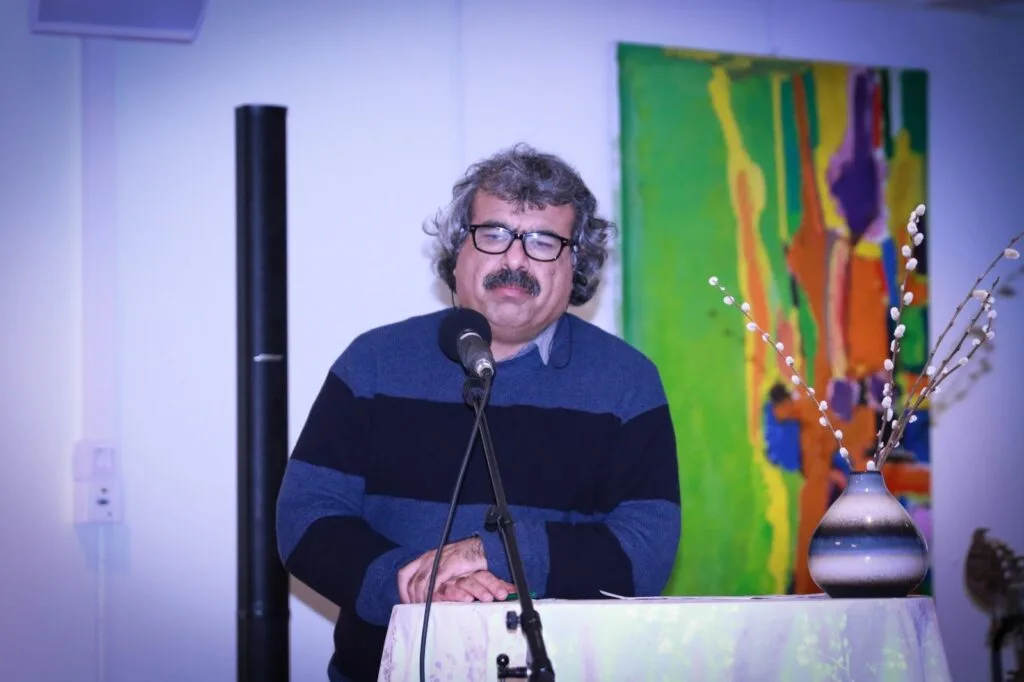 Pashto Music Institute Launches in Malmö, Sweden, Heralding a New Era of Musical Heritage Preservation Ghafoor Liwal, a cultural scholar, speaking at the Pashto Music Institute's launch. He stands at a podium, with a colorful painting and decorative vase in the background.