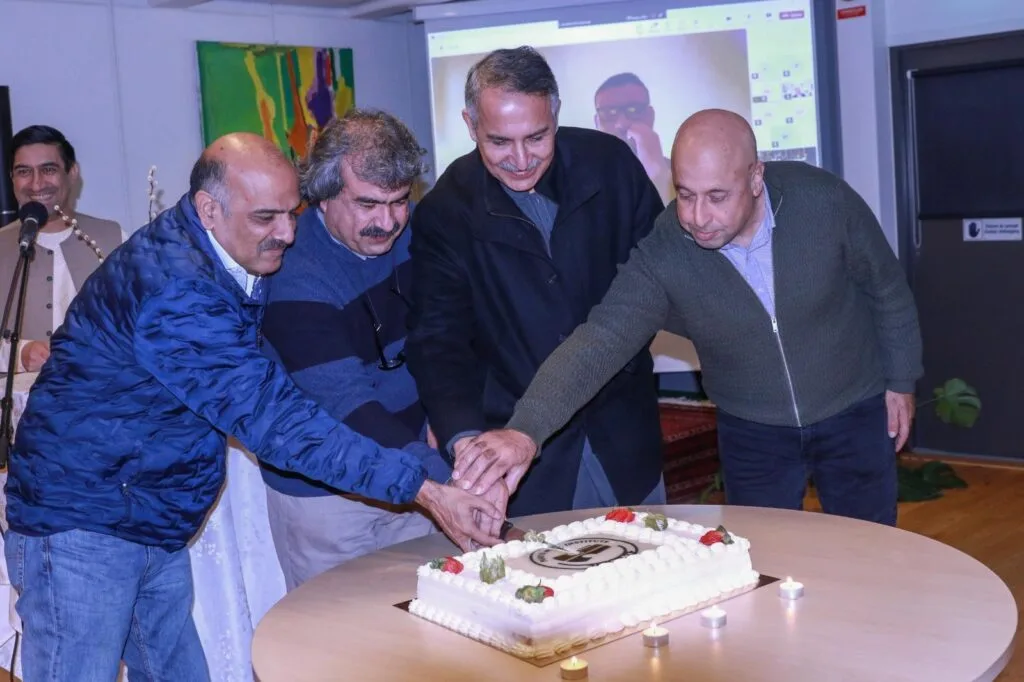 Pashto Music Institute Launches in Malmö, Sweden, Heralding a New Era of Musical Heritage Preservation Haroon Bacha and other organizers cutting a cake during the Pashto Music Institute's soft launch event. A screen displaying a video call is visible in the background.