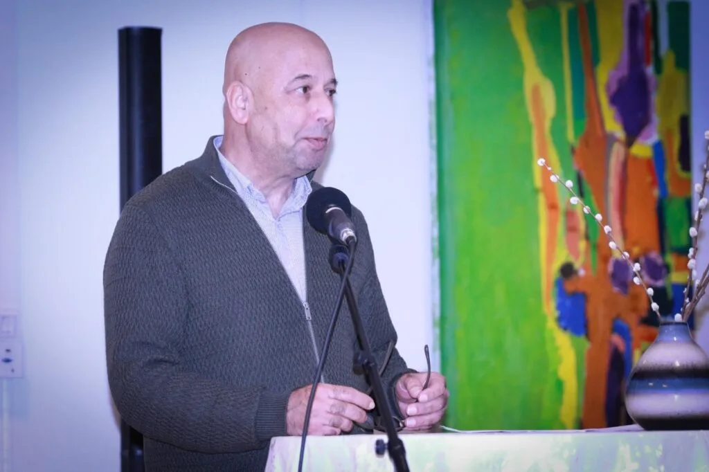 Pashto Music Institute Launches in Malmö, Sweden, Heralding a New Era of Musical Heritage Preservation Abdul Malik Bekasyar, a well-known Afghan poet, speaking at the podium during the Pashto Music Institute's launch event. A colorful painting and a decorative vase are visible in the background.