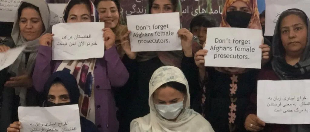 Afghan Women Prosecutors in Pakistan Protest Forced Deportations A group of Afghan women prosecutors hold signs in Persian and English, calling on the Pakistani government to stop the expulsion of Afghan refugees. Some women wear headscarves, while others wear masks, standing in front of banners related to legal and human rights organizations.