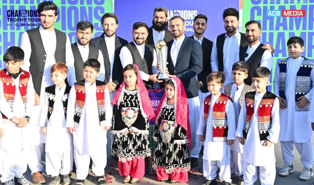 Afghan Cricket Fans Struggle to Obtain Pakistani Visas for Champions Trophy Afghan cricket players with the ICC Champions Trophy, accompanied by children in traditional Afghan clothing, during the December 2024 trophy tour.