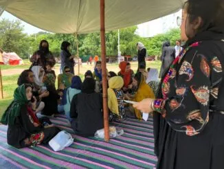 A group of Afghan women sitting under a tent in Islamabad, engaging in discussions about their rights and future.