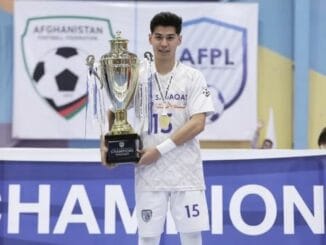 Afghan Player Mehran Ghulami Nominated for Best Men's Young Player in Futsal Mehran Ghulami holding a championship trophy in his futsal uniform, with the Afghanistan Football Federation and AFPL banners in the background.
