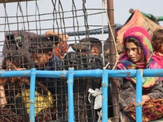 A group of Afghan children and women inside a truck with metal fencing at the Torkham border crossing on October 31, 2023. A young girl in a colorful headscarf gazes outside, while others, including small children, look through the bars of the truck. The uncertainty and hardship of their forced return are visible in their expressions.