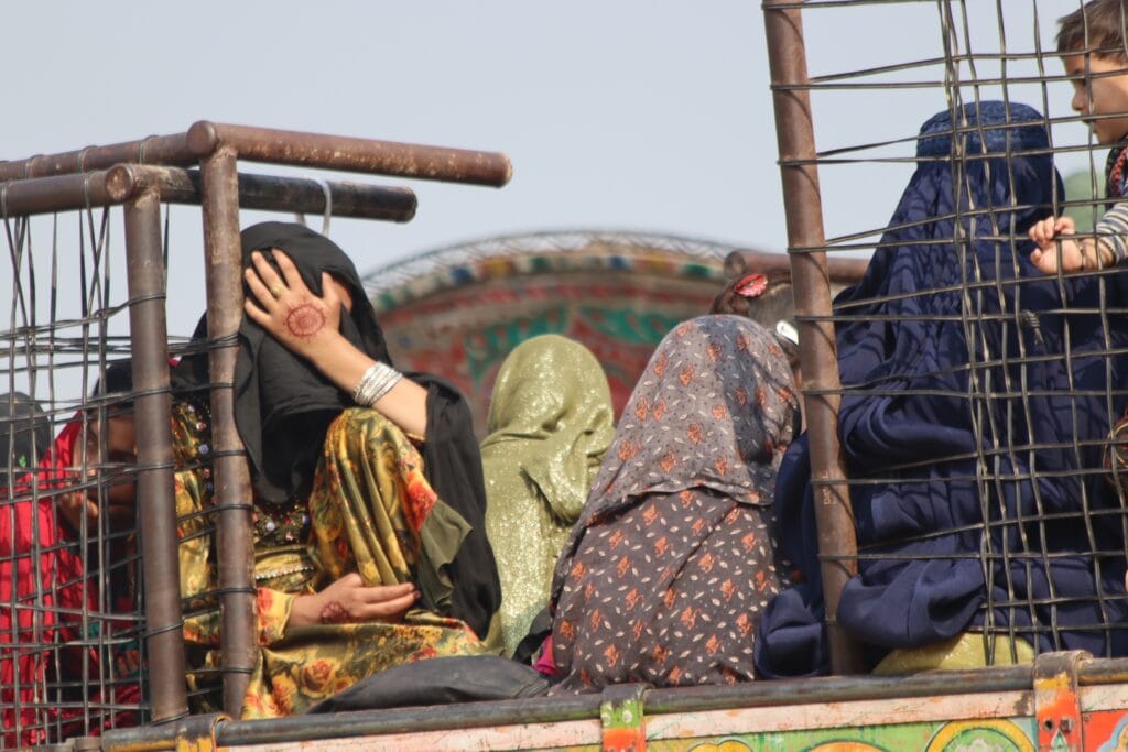 A group of Afghan women and children sit inside a truck with metal bars at the Torkham border crossing, returning from Pakistan to Afghanistan on October 31, 2023. Some women cover their faces with scarves, while others wear traditional clothing, reflecting the uncertainty of their journey.