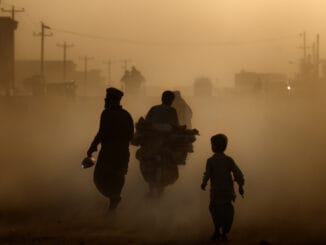 A hazy street in Kabul, Afghanistan, showing people walking and cycling through thick air pollution, highlighting severe environmental conditions.