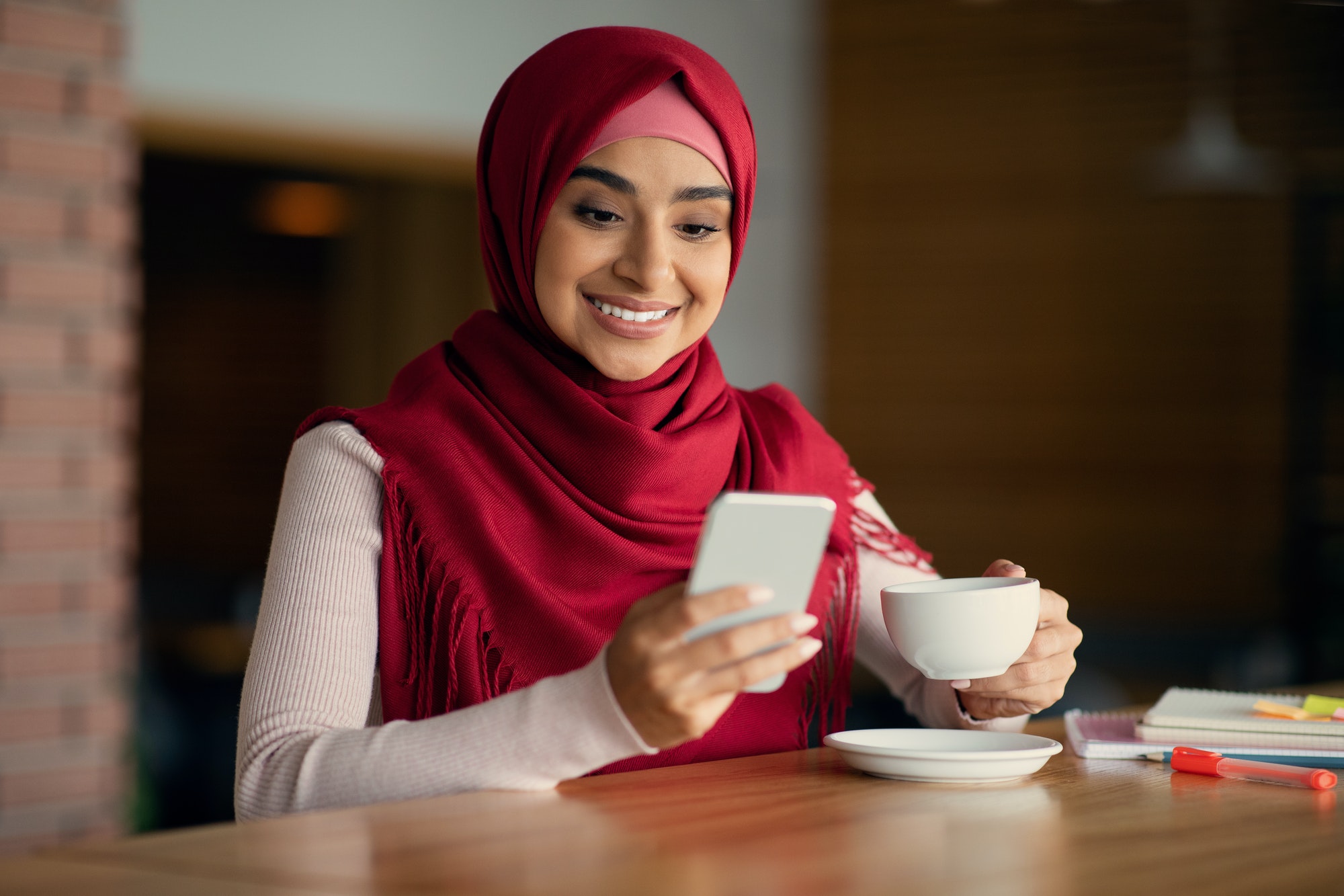 Happy muslim lady SMM-manager using mobile phone at cafe